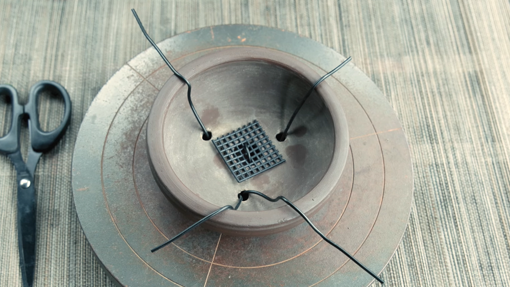 Tie-down wire threaded through the holes of a bonsai pot